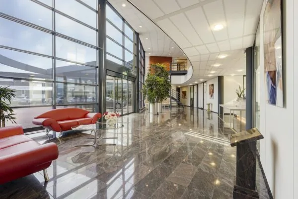 Moderne en ruim opgezette entreehal aan de Laan van ‘s-Gravenmade met glazen gevel, rode designbanken en glanzende marmeren vloer.